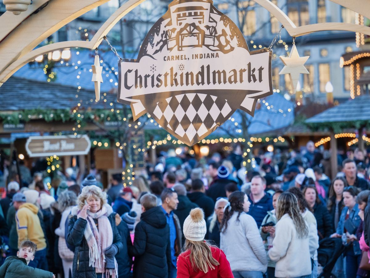 A crowd gathers under a welcoming archway at the Carmel, Indiana Christkindlmarkt, adorned with festive lights and decorations.
