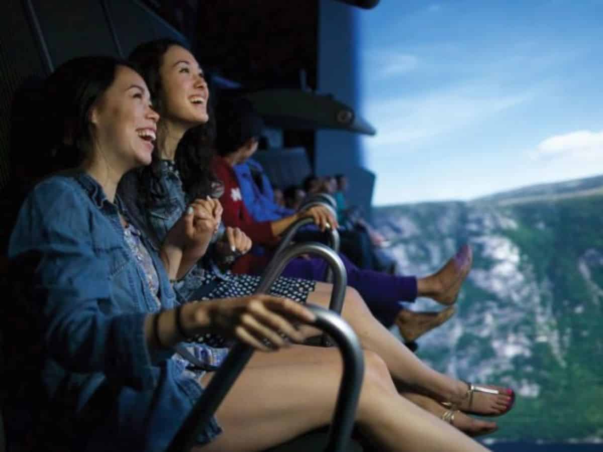 A group of people sitting on a roller coaster in front of a mountain at the Mall of America.