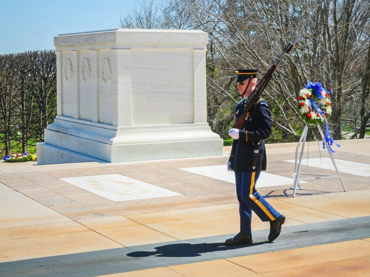 A soldier in uniform guards the Tomb of the Unknown Soldier at Arlington National Cemetery. A wreath is placed nearby.